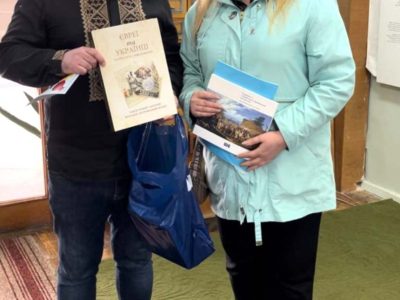 Vladyslav Hrynevych, Jr., UJE's regional manager in Ukraine, presents Olena Chervinska, head of Kaniv's Jewish community, with a set of books published with UJE support. Kaniv, 31 October 2025.