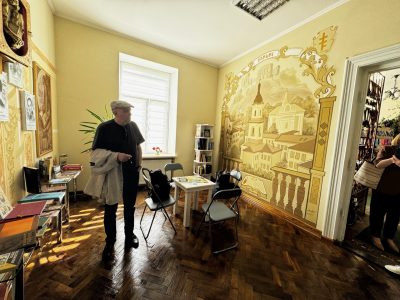Василь Махно в міській бібліотеці Бучача на тлі муралу з зображенням міста.