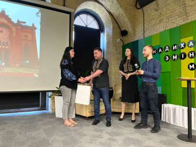 Vladyslav Hrynevych, Jr., regional manager of UJE, presents a diploma and gifts to Marianna Bychkova, the Jewish Heritage 2022 category winner of the Wiki Loves Monuments photography competition. Kyiv, 20 May 2023.